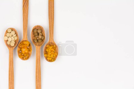 Dietary supplement capsules and herbal pills on wooden spoons, top view with copy space