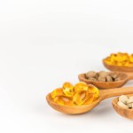 Close-up of wooden spoons with capsules and dietary supplement pills on white background, copy space