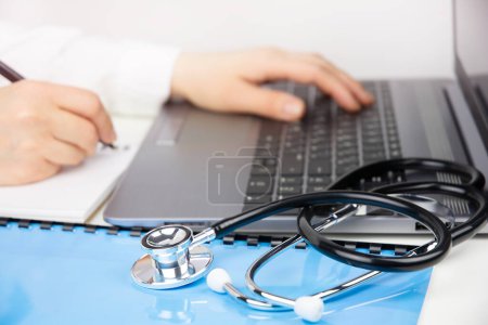 Doctor working in modern medical office, making notes and using laptop. Medical education and online medicine concept