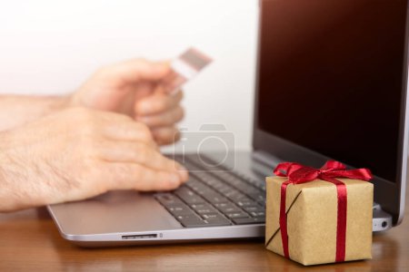 Foto de Caja de regalo cerca del ordenador portátil, hombre usando el ordenador portátil y la celebración de la tarjeta de crédito. Concepto de compras online - Imagen libre de derechos