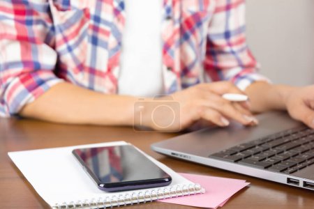 Foto de Lugar de trabajo. Mujer usando el ordenador portátil en la mesa con notas y teléfono inteligente. Trabajar en casa concepto - Imagen libre de derechos