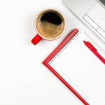 Red coffee cup with red notepad and pen, laptop keyboard on white background. Top view with copy space