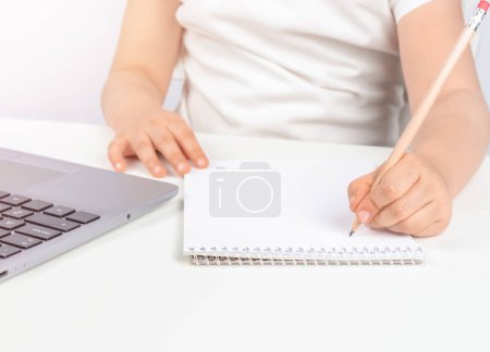 Foto de Niño está escribiendo en el bloc de notas contra el ordenador portátil, espacio para copiar - Imagen libre de derechos