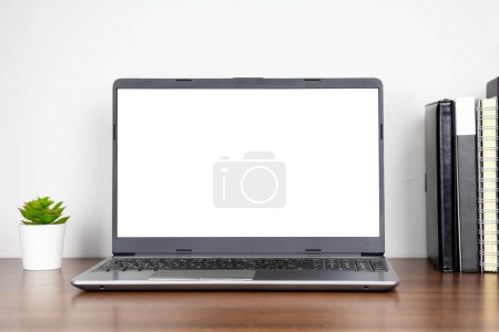 Foto de Hogar lugar de trabajo con portátil de pantalla en blanco y libros sobre mesa de madera con fondo de pared blanco - Imagen libre de derechos