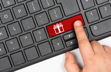 Foto de Concepto de compras navideñas online. Childs dedo presionando la tecla roja en el teclado de la computadora con símbolo de caja de regalo - Imagen libre de derechos