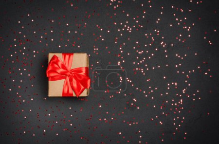 Foto de Caja de regalo con cinta roja sobre fondo negro con estrellas brillantes confeti, vista superior con espacio para copiar. Concepto de celebración - Imagen libre de derechos