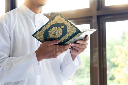 Muslimischer Mann liest den heiligen Koran. Heiliger Koran in der Hand mit arabischer Textbedeutung des Al Qur 'an