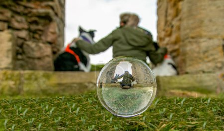 Photo for Photograph taken through a photography glass ball of girl in green jacket sitting with her two dogs in an old stone doorway - Royalty Free Image