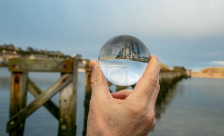 Téléchargez les photos : Photographie boule de verre dans la main humaine photographie un vieux pont en bois au soleil au bord de la mer, abstrait, artistique, à l'envers, concept intéressant - en image libre de droit