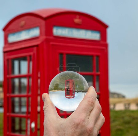 Téléchargez les photos : Cabine téléphonique rouge photographiée à travers une bille de verre - en image libre de droit