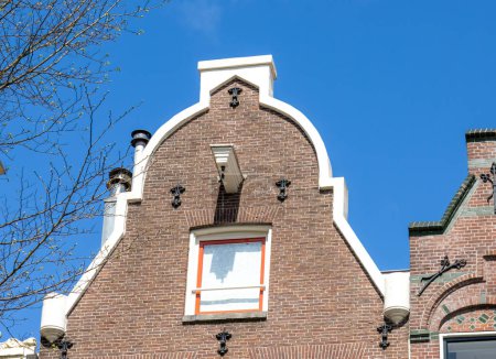 Téléchargez les photos : Anciennes maisons de ville traditionnelles et historiques d'Amsterdam sur les rives des canaux avec porte-à-faux et crochets sur les pignons avant des maisons étroites inclinées au printemps avec un beau ciel bleu - en image libre de droit