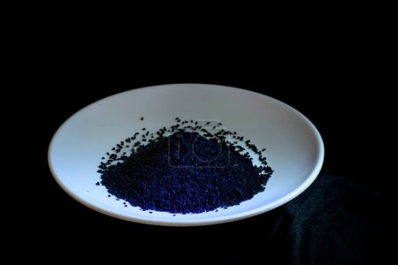 Téléchargez les photos : Une poignée de graines de cumin noir sur une assiette blanche sur un fond noir - en image libre de droit