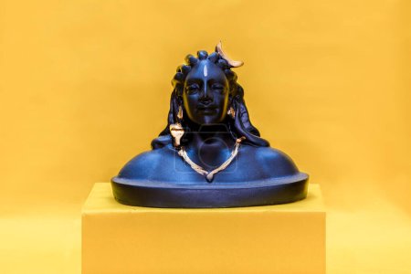 Version miniature de l'idole Adiyogi Shiva assise sur une boîte jaune et fond jaune