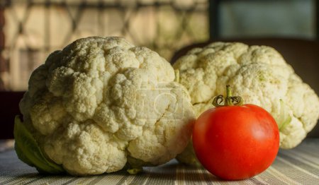Photo for Red tomato placed on a a table mat with out focus cauliflowers in the background closeup food photo - Royalty Free Image
