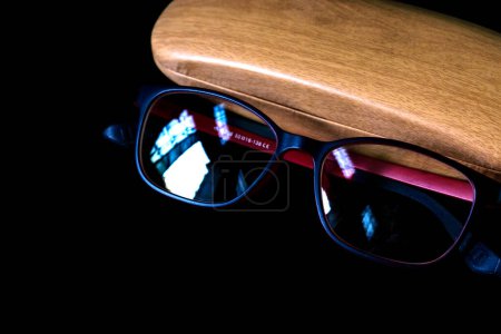 Téléchargez les photos : Lunettes à monture rouge avec son étui en bois sur le dessus du miroir réfléchissant noir - en image libre de droit