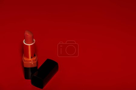 Téléchargez les photos : Le rouge à lèvres rouge est ouvert sur la table rouge avec son couvercle noir de côté photographie de produit - en image libre de droit