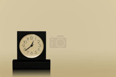 Téléchargez les photos : Horloge de table noire avec cadran blanc debout sur la table sombre isolé sur fond sombre - en image libre de droit