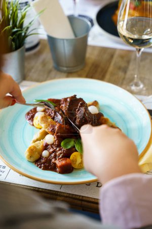 Téléchargez les photos : Une personne qui mange du bœuf cuit avec des légumes sur une table en bois - en image libre de droit