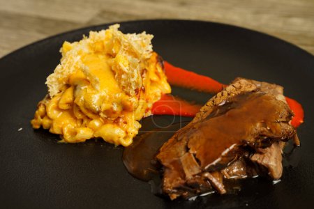 Slices of meat with mac and cheese on a black plate