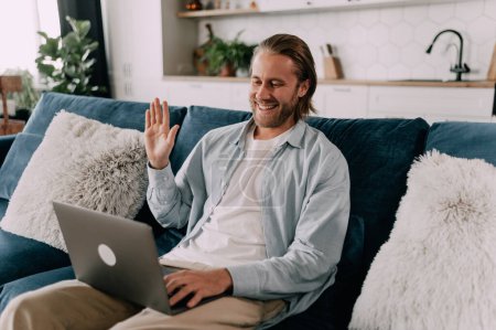 Foto de Conversación en línea sosteniendo un portátil. Un hombre está saludando a una pantalla de su portátil con una sonrisa - Imagen libre de derechos