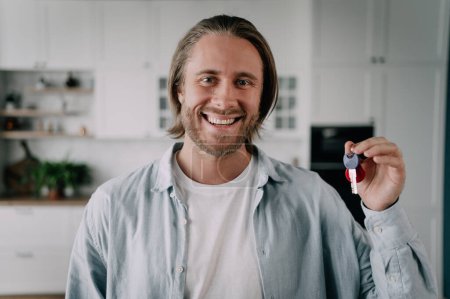 Téléchargez les photos : Un agent immobilier masculin montrant la clé et regardant une caméra avec un sourire attirer les clients avec une bonne offre. - en image libre de droit