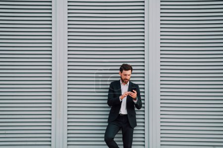 Photo for Businessman use phone app on brick wall background. empty space for text. Business man holding smartphone in suit. Urban young professional lifestyle - Royalty Free Image