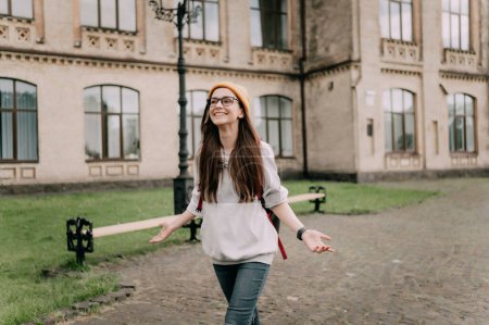 Téléchargez les photos : Heureuse étudiante caucasienne marchant autour du campus souriant à la caméra - en image libre de droit
