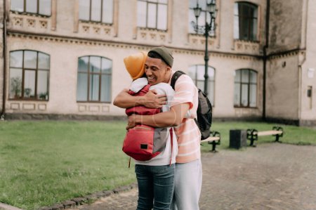Téléchargez les photos : Un homme afro-américain de 20 ans et des amies se sont rencontrées dans la rue et se sont embrassées. Amitié internationale adolescent. - en image libre de droit