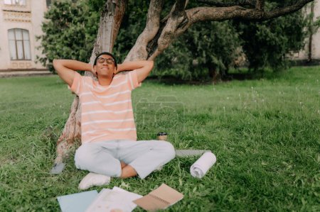 Photo for General scene of a campus life. Focus on african American student with glasses putting down his books and relaxing with his eyes closed. - Royalty Free Image