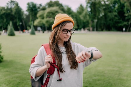 Photo for Stylish young woman in Casual looks in Smart Watch on the background of a city park. - Royalty Free Image
