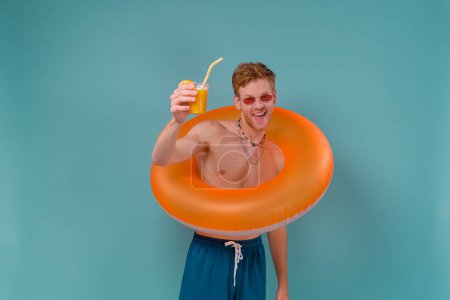 Téléchargez les photos : Beau jeune homme de sauveteur drôle en maillot de bain se détendre tenir anneau gonflable sur fond bleu vacances d'été soleil de mer bronzage concept sur fond bleu. - en image libre de droit