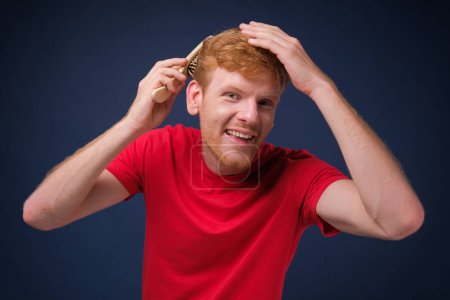 Photo for A handsome confident man combing his hair on a blue background. - Royalty Free Image