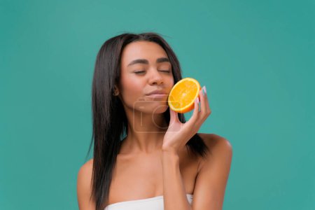 Téléchargez les photos : Attrayant afro-américain fille ayant piec d'orange, profiter de l'odeur fraîcheur avec sourire sur le fond bleu. - en image libre de droit