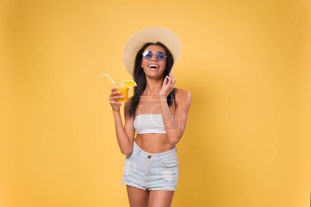 Foto de Feliz mujer afroamericana bebiendo un cóctel divirtiéndose. Concepto de vacaciones de verano. aislado sobre fondo amarillo - Imagen libre de derechos