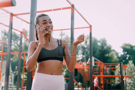 Téléchargez les photos : Photo d'une sportive afro-américaine souriante parlant sur un téléphone portable sur un terrain de sport. - en image libre de droit