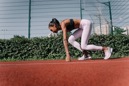 Foto de Atleta femenina segura en posición inicial lista para correr. Joven mujer a punto de empezar un sprint. - Imagen libre de derechos