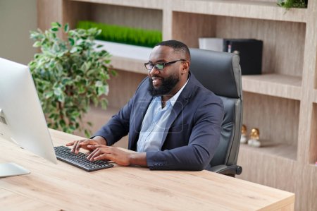 Foto de Hombre de negocios afroamericano usando computadora durante el trabajo en la oficina. Concepto de hombre moderno y exitoso - Imagen libre de derechos
