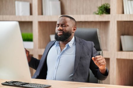 Photo for African American in business suit office worker gets uncomfortable in his office chair and sour back muscles. - Royalty Free Image