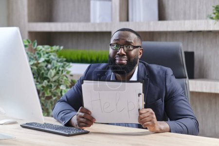 Téléchargez les photos : Jeune homme d'affaires malheureux assis et tenant le drapeau blanc avec l'aide de texte au bureau - en image libre de droit