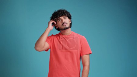 Téléchargez les photos : Homme indien en corail t-shirt sur fond bleu studio réflexion à la recherche d'une idée - en image libre de droit