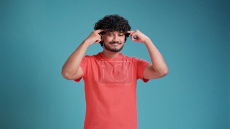 Foto de Hombre indio señalando con el dedo su cabeza mostrando alto intelecto y buenos cerebros y capacidad de pensar en camiseta de coral sobre fondo azul del estudio - Imagen libre de derechos