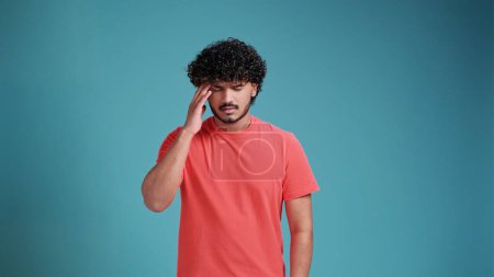 Photo for Young handsome Indian man wearing in coral t-shirt on blue studio background with hand on head for pain in head. Suffering migraine - Royalty Free Image