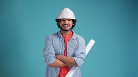 Téléchargez les photos : Les gens et le concept de travail. Un architecte de construction indien ou arabe positif porte un casque rigide et sourit volontiers à la caméra isolée sur fond bleu - en image libre de droit