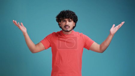 Photo for I don't know, who cares. Portrait of confused clueless brunette latin spanish man shrugging shoulders, making no idea gesture, whatever. isolated on a blue studio background. - Royalty Free Image