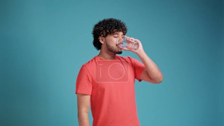 Photo for Handsome hispanic man drinking a glass of fresh water against blue background - Royalty Free Image