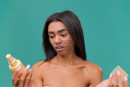 Foto de Mujer joven afroamericana muestra decepción con una crema. Retroalimentación negativa sobre el fondo turquesa. - Imagen libre de derechos