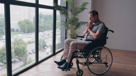 Téléchargez les photos : Un homme âgé en fauteuil roulant prie près de la fenêtre de la clinique - en image libre de droit