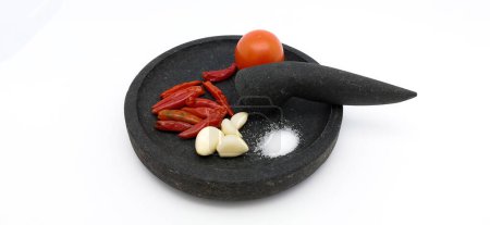 Foto de Chiles rojos, ajos, tomate y sal en artículos de piedra, ingredientes para hacer tomate sambal tradicional indonesio o salsa de tomate picante. Aislado sobre fondo blanco. - Imagen libre de derechos