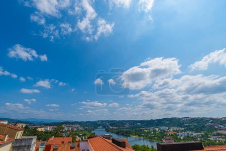 A view of Coimbra City under a beautiful clear sky, with Mondego River, trees, and buildings. Landscape background and wallpaper.