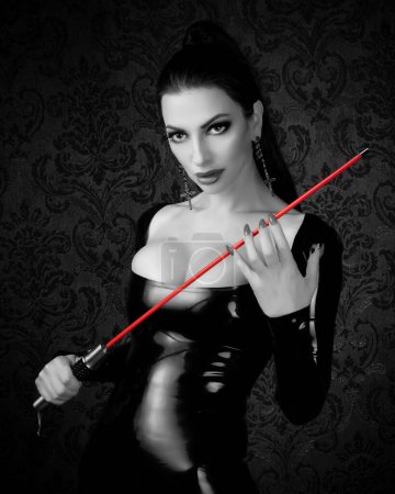 Téléchargez les photos : Portrait de femme dominante aux gros seins sexy en catsuit fétiche en latex taille basse avec fouet noir et blanc sauf pour le fouet rouge et les ongles - en image libre de droit